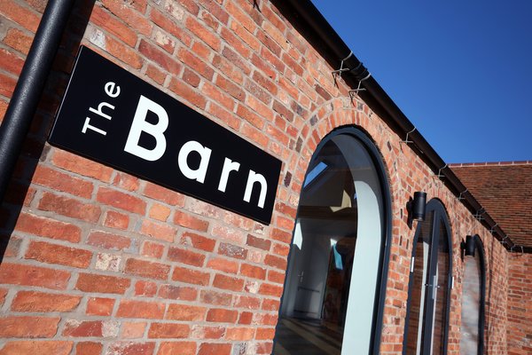 Photograph taken from ground level showing the front door sign of The Barn and the arched windows and doors.